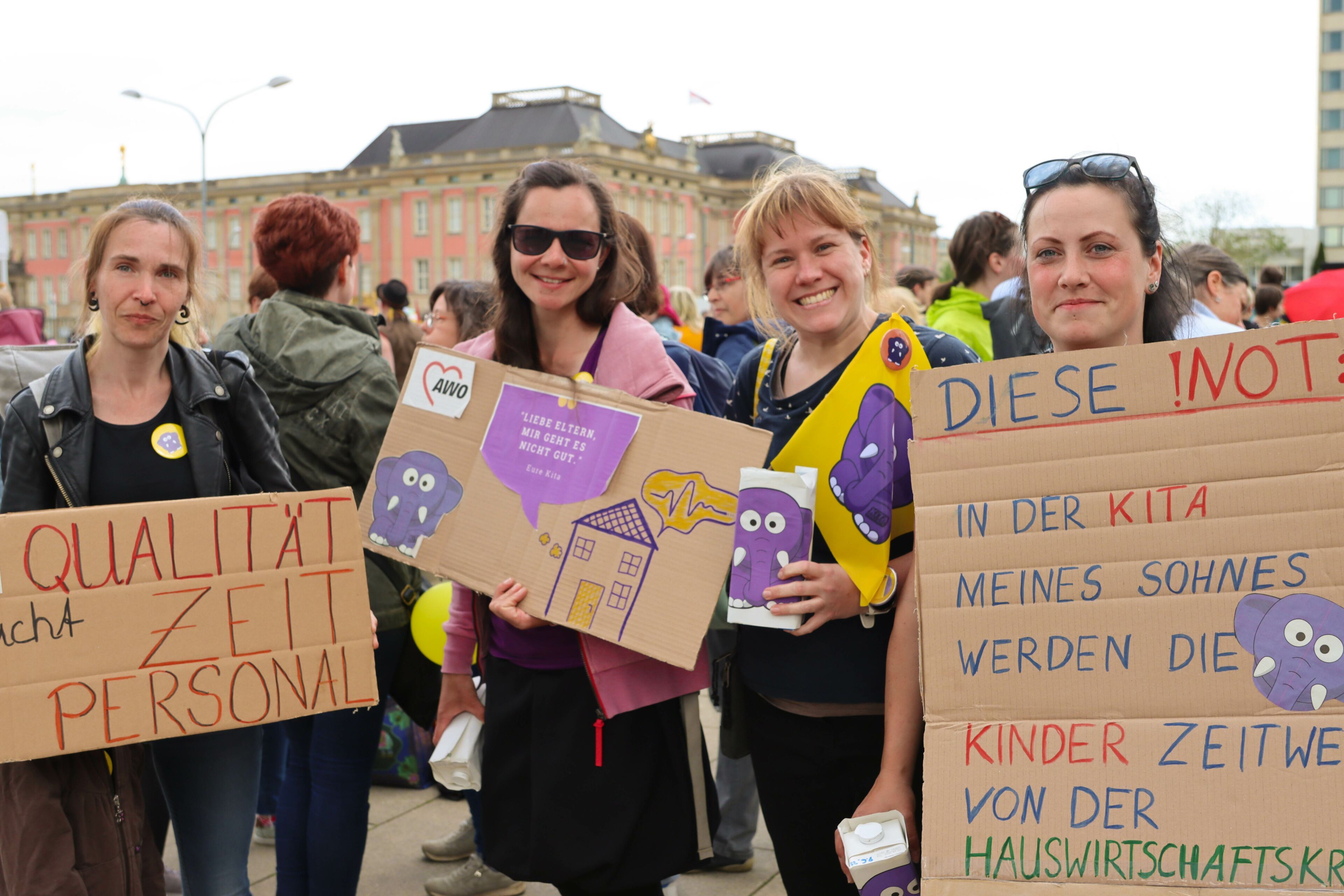 Der Landtag Brandenburg im Hintergrund. 4 Frauen mit Plakaten auf einer Demonstration. Die Frauen halten ihre Plakate in die Kamera und lächeln.