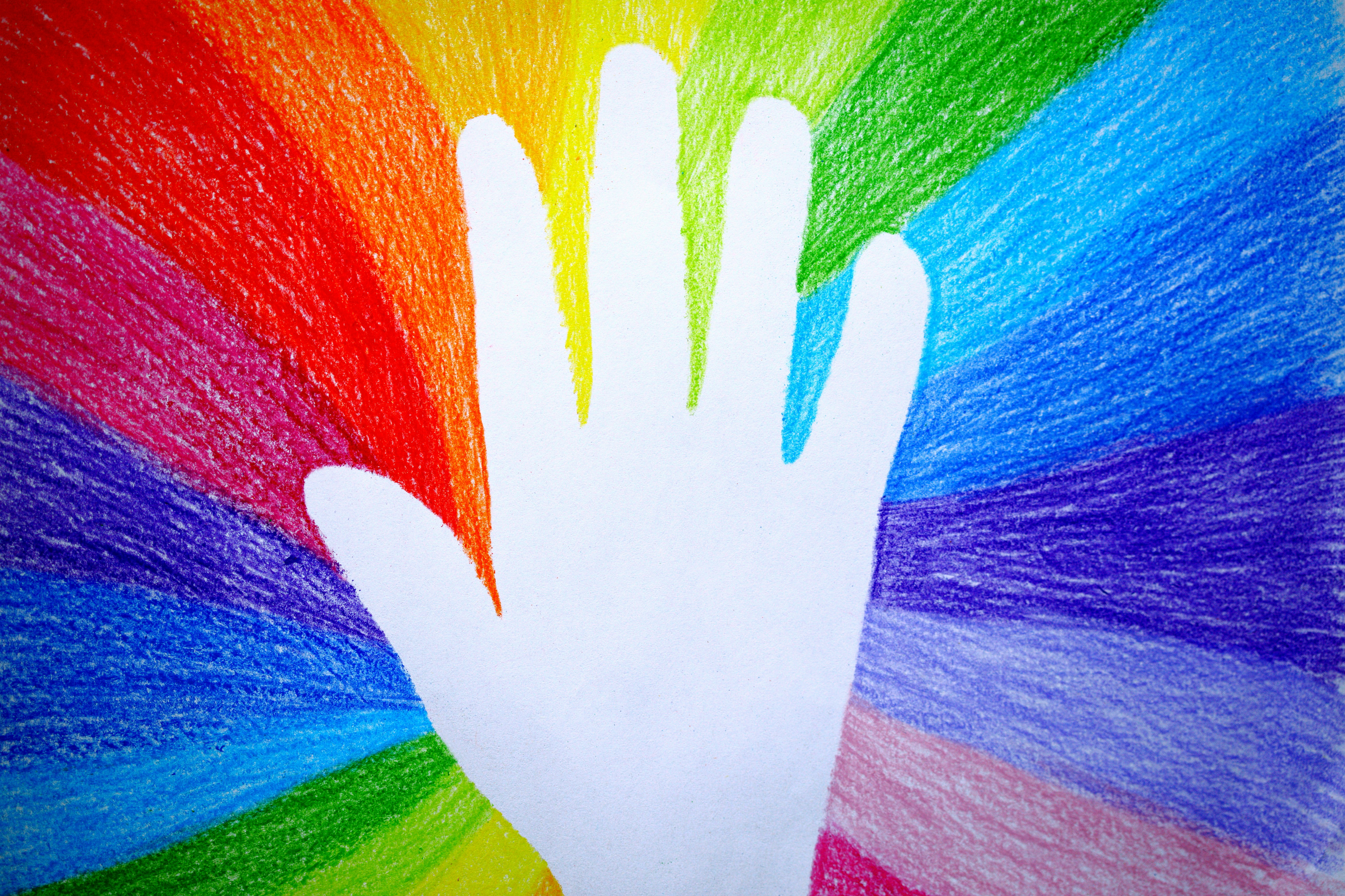 Ein mit Buntstiften gemaltes Bild mit weißer Hand in der Mitte, von der ringsherum Regenbogenfarben abstrahlen.